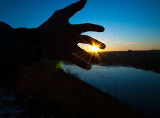 Silhouette of hands on a background of blue sky sunset. The rays of the sun through your fingers.