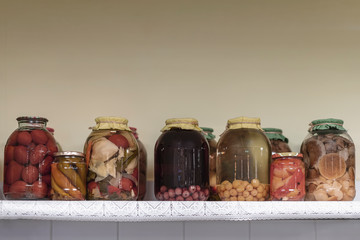 Handmade preserved fruits, vegetables and mushrooms on a long shelf with a napkin, background