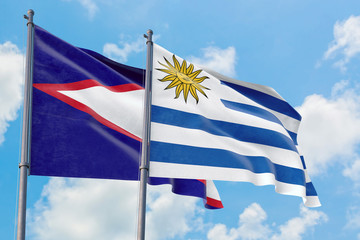 Uruguay and American Samoa flags waving in the wind against white cloudy blue sky together. Diplomacy concept, international relations.
