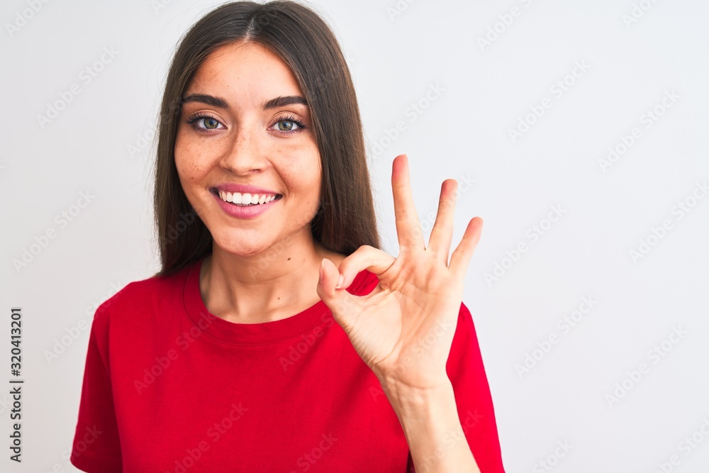Wall mural Young beautiful woman wearing red casual t-shirt standing over isolated white background doing ok sign with fingers, excellent symbol - Wall murals