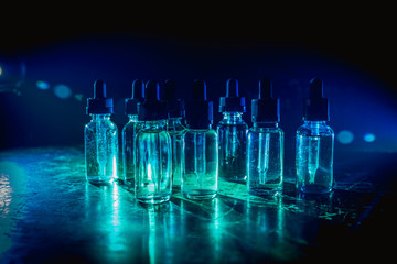 Smoke clouds and vape liquid bottles on dark background. Light effects. Useful as background or vape advertisement or vape background. Selective focus