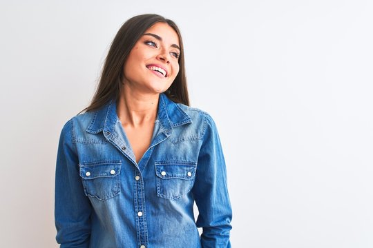 Young beautiful woman wearing casual denim shirt standing over isolated white background looking away to side with smile on face, natural expression. Laughing confident.