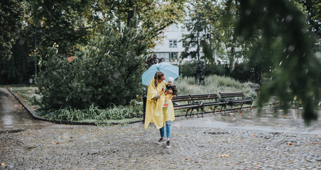 Beautiful and happy middle age woman with her baby walking in city park on rainy day..
