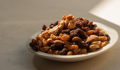  Image of walnut, hand, raisins and almonds on a white plate with natural light.