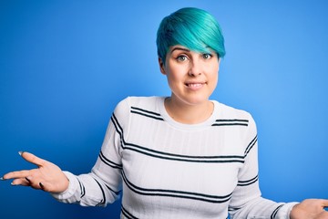Young beautiful woman with blue fashion hair wearing casual sweater standing at studio clueless and...