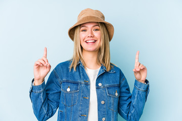 Young blonde caucasian woman isolated indicates with both fore fingers up showing a blank space.