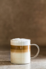 A glass of caffe latte macchiato coffee, vertical with brown background.