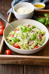 Fusilli pasta with basil pesto sauce and cherry tomatoes, sprinkled with shredded cheese