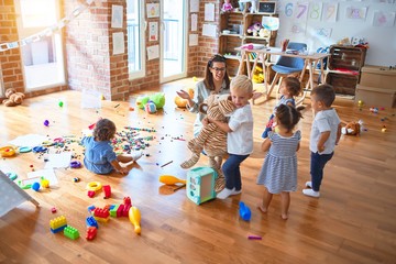 Beautiful teacher and group of toddlers playing around lots of toys at kindergarten