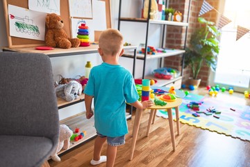 Young caucasian kid playing at kindergarten with toys. Preschooler boy happy at playroom.