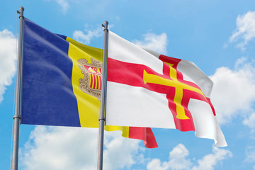 Guernsey and Andorra flags waving in the wind against white cloudy blue sky together. Diplomacy concept, international relations.