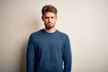 Young handsome man with beard wearing casual sweater standing over white background depressed and worry for distress, crying angry and afraid. Sad expression.