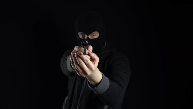 A man in a balaclava mask stands with a gun. A thug points his gun at the camera. On a black background.