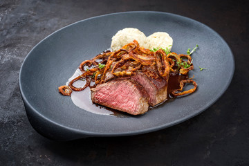 Traditioneller dry aged Zwiebelrostbraten aufgeschnitten vom Rind mit gebratenen Zwiebelringen, Kartoffleknödel und würtige Bratensauce serviert als closeup auf einem Modern Design Teller