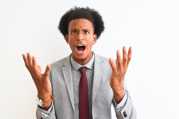 Young african american businessman wearing suit standing over isolated white background crazy and...
