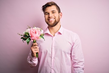 Young blond romantic man with beard and blue eyes holding beautiful bouquet of flowers with a happy face standing and smiling with a confident smile showing teeth