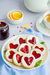 Linzer cookies with heart with raspberry jam and powdered sugar on a white plate with a cup of tea. Dessert on Valentine's Day. Vertical orientation