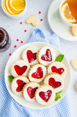 Linzer cookies with heart with raspberry jam and powdered sugar on a white plate with a cup of tea. Dessert on Valentine's Day. Vertical orientation. Top view