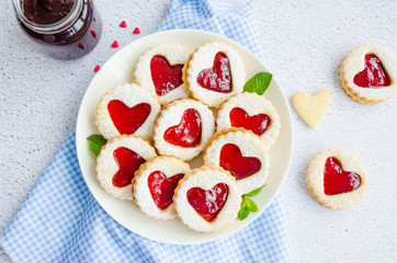 Linzer cookies with heart with raspberry jam and powdered sugar on a white plate with a cup of tea. Dessert on Valentine's Day. Horizontal orientation, top view
