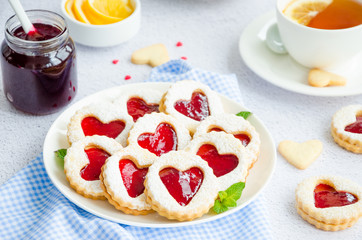 Linzer cookies with heart with raspberry jam and powdered sugar on a white plate with a cup of tea. Dessert on Valentine's Day. Horizontal orientation