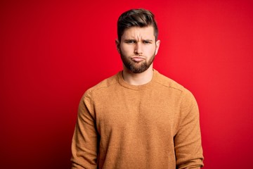 Young blond man with beard and blue eyes wearing casual shirt over red background depressed and worry for distress, crying angry and afraid. Sad expression.