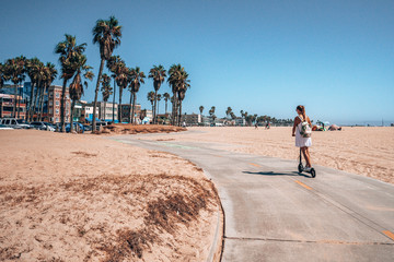 Beautiful girl riding an electric scooter down the Venice beach bike lane, along the beach and the...