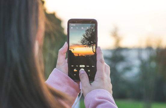 Female persons hands are holding the smartphone and taking a photo of the sunset. Smartphone photography.