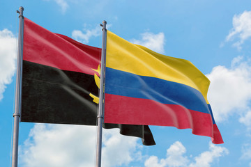 Colombia and Angola flags waving in the wind against white cloudy blue sky together. Diplomacy concept, international relations.