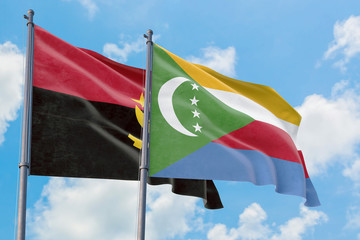 Comoros and Angola flags waving in the wind against white cloudy blue sky together. Diplomacy...