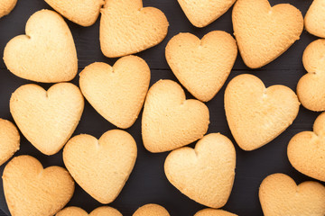 Heart shaped cookies decorated for Valentine's Day. Free space for text. Wooden plate with heart shaped cookies on a black wooden table