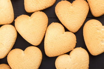 Heart shaped cookies decorated for Valentine's Day. Free space for text. Wooden plate with heart shaped cookies on a black wooden table