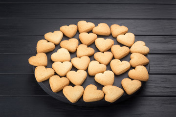 Heart shaped cookies decorated for Valentine's Day. Free space for text. Wooden plate with heart shaped cookies on a black wooden table