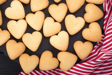 Heart shaped cookies decorated for Valentine's Day. Free space for text. Wooden plate with heart shaped cookies on a black wooden table