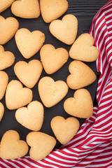 Heart shaped cookies decorated for Valentine's Day. Free space for text. Wooden plate with heart shaped cookies on a black wooden table