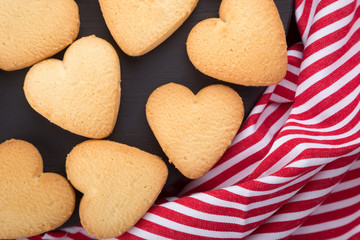 Heart shaped cookies decorated for Valentine's Day. Free space for text. Wooden plate with heart shaped cookies on a black wooden table