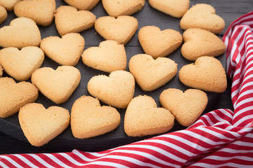 Heart shaped cookies decorated for Valentine's Day. Free space for text. Wooden plate with heart shaped cookies on a black wooden table