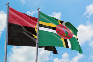 Dominica and Angola flags waving in the wind against white cloudy blue sky together. Diplomacy...