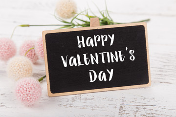 Small chalkboard for Valentine's day. Background with pink roses on old wooden table.