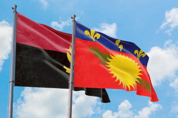 Guadeloupe and Angola flags waving in the wind against white cloudy blue sky together. Diplomacy concept, international relations.