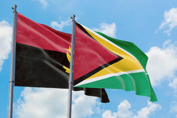 Guyana and Angola flags waving in the wind against white cloudy blue sky together. Diplomacy concept, international relations.