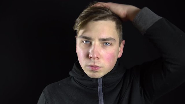 A young man takes off the mask of a balaclava. Bandit on a black background close-up.