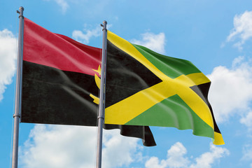 Jamaica and Angola flags waving in the wind against white cloudy blue sky together. Diplomacy concept, international relations.