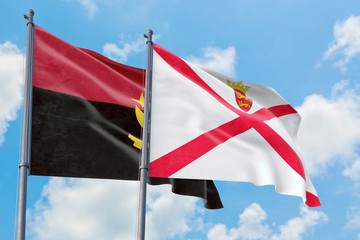 Jersey and Angola flags waving in the wind against white cloudy blue sky together. Diplomacy concept, international relations.