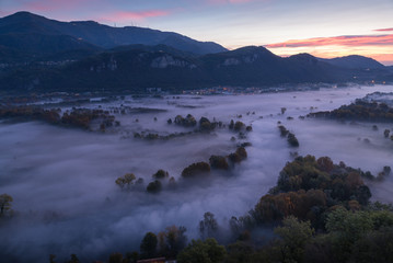 Abstract with Airuno on Adda river in Italy at sunrise with myst fog trees foliage in autumn fall season