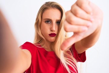 Young beautiful woman wearing t-shirt make selfie by camera over isolated white background with angry face, negative sign showing dislike with thumbs down, rejection concept
