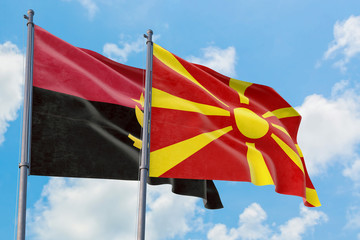 Macedonia and Angola flags waving in the wind against white cloudy blue sky together. Diplomacy concept, international relations.