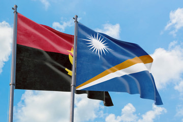 Marshall Islands and Angola flags waving in the wind against white cloudy blue sky together....