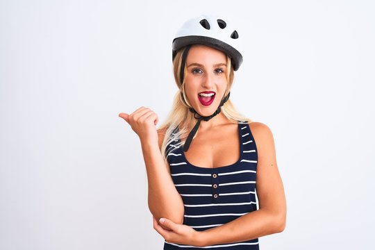 Young beautiful woman wearing bike helmet standing over isolated white background smiling with happy face looking and pointing to the side with thumb up.