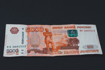 One Russian bill in the amount of 5000 rubles lies on a black background.