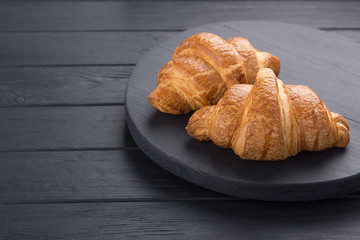 Croissants on a black wooden table. Croissant breakfast. Croissants on a wooden board and a black wooden table. Fresh French Baked Croissants. Warm Fresh Buttery Rolls. Free space for text.